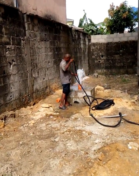 Two crew members maintaining a borehole, fitting a blue casing pipe at a muddy drilling site
